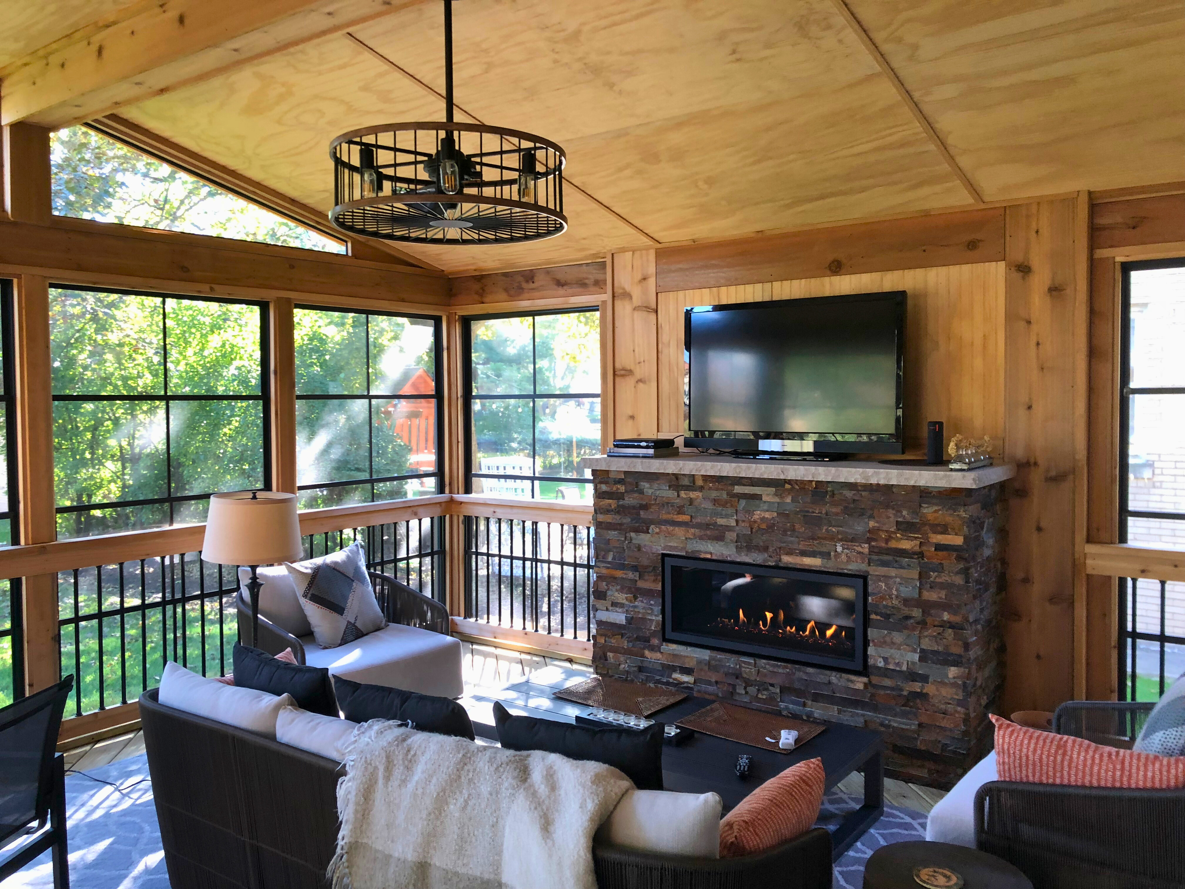 Inside of a three-season-room with 4-track windows, a fireplace, and cozy furniture.