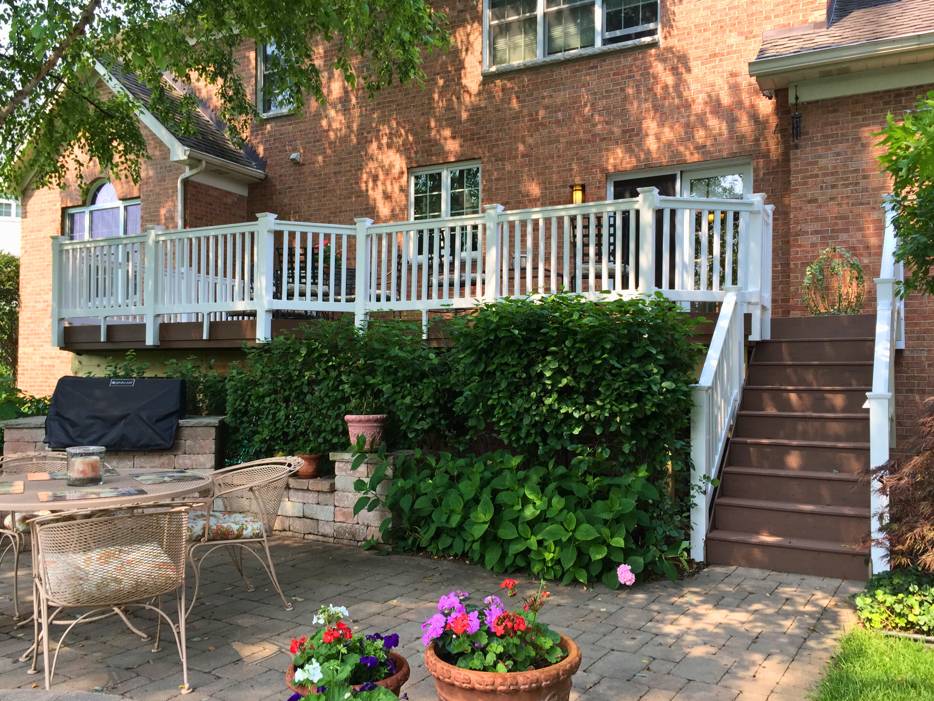 Elevated brown composite deck with white rails and stairs down to a paver patio.