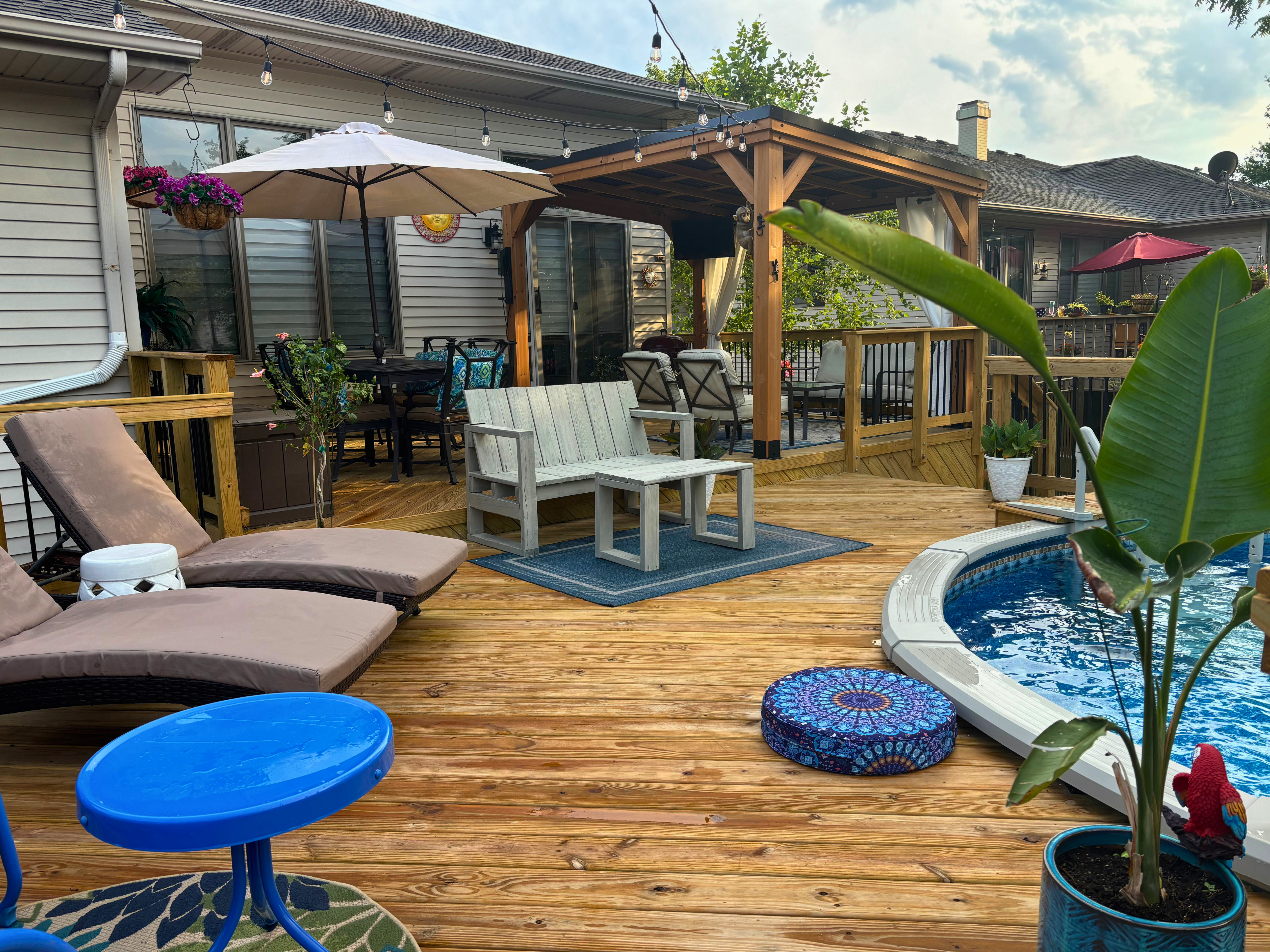 Custom wood pool deck with outdoor furniture, umbrella, and open porch in Plainfield, IL.