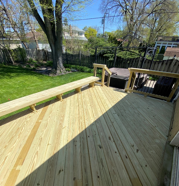 Custom light-wood deck featuring an integrated bench railing and built-in spa in a wooded backyard.