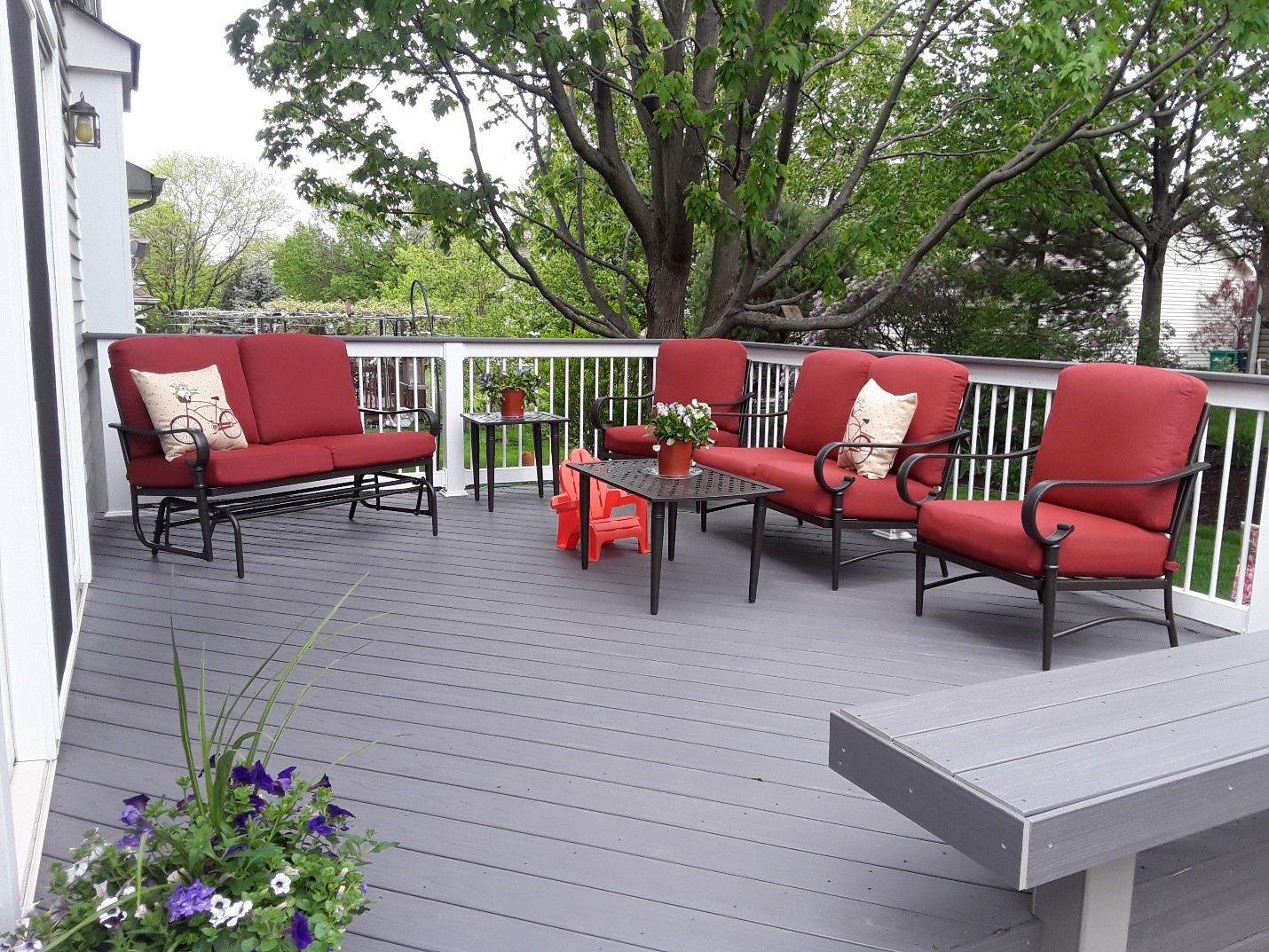 Grey composite deck with white rails, built-in bench, and outdoor furniture with red cushions.