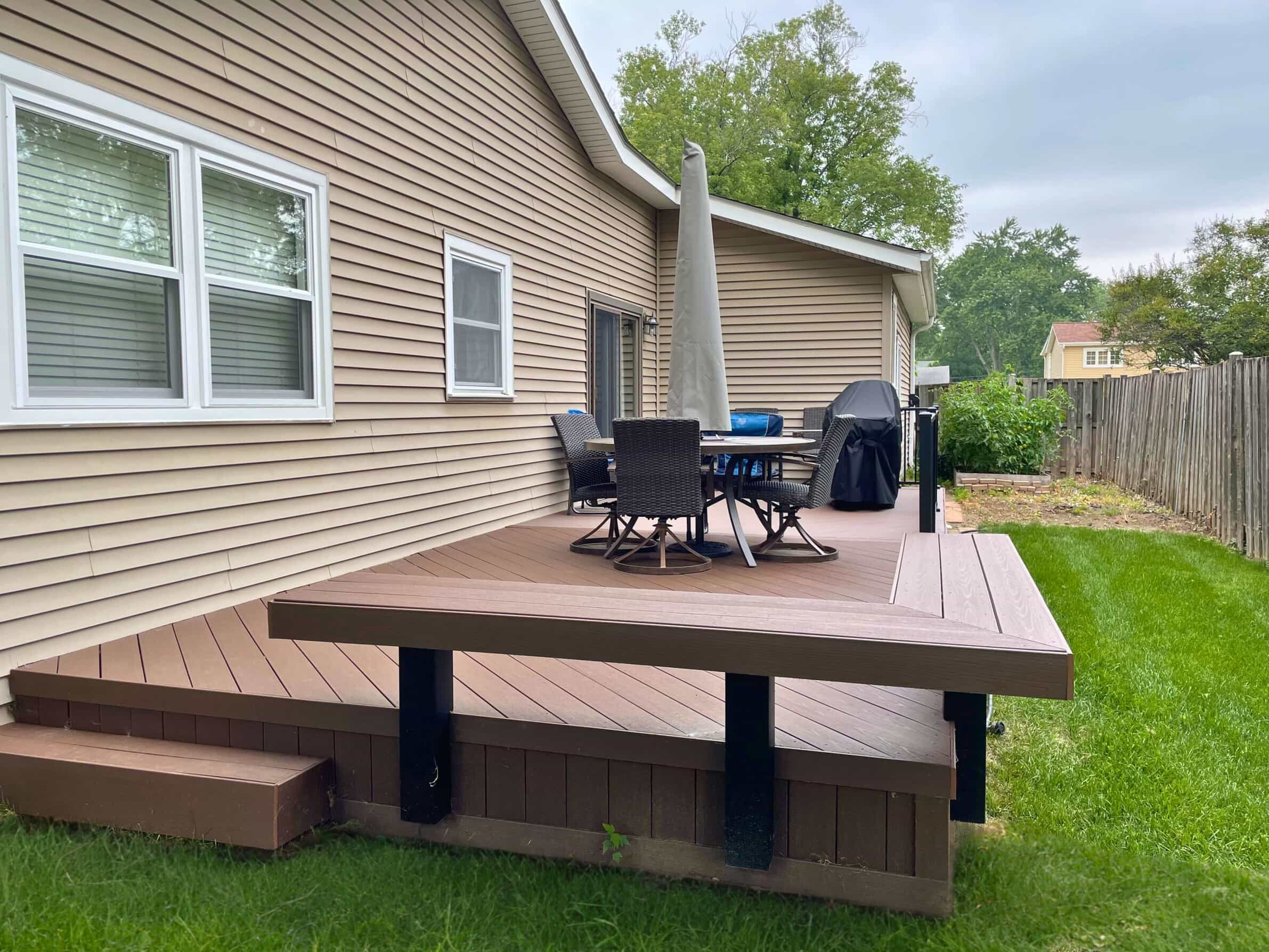 Custom low-profile composite deck with brown decking, black railings, and outdoor furniture next to a tan siding house in Tinley Park, IL.