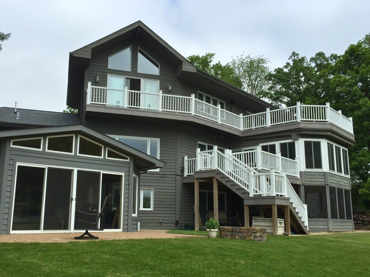 A large multi-level home with a gray exterior and white railings, featuring multiple decks and a walkout basement covered porch, set against a backdrop of trees in Hawthorn Woods, Illinois.