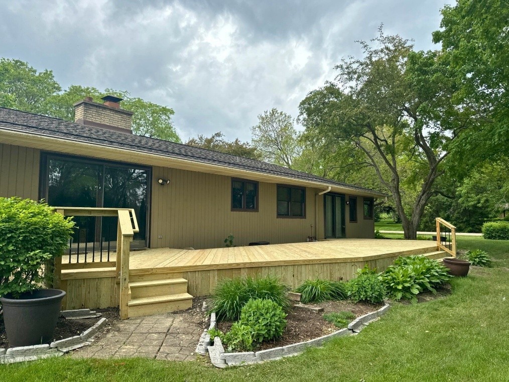 A newly built, spacious wooden deck with steps leading to a well-maintained garden, attached to a light brown house, with a cloudy sky overhead in Hawthorn Woods, Illinois.