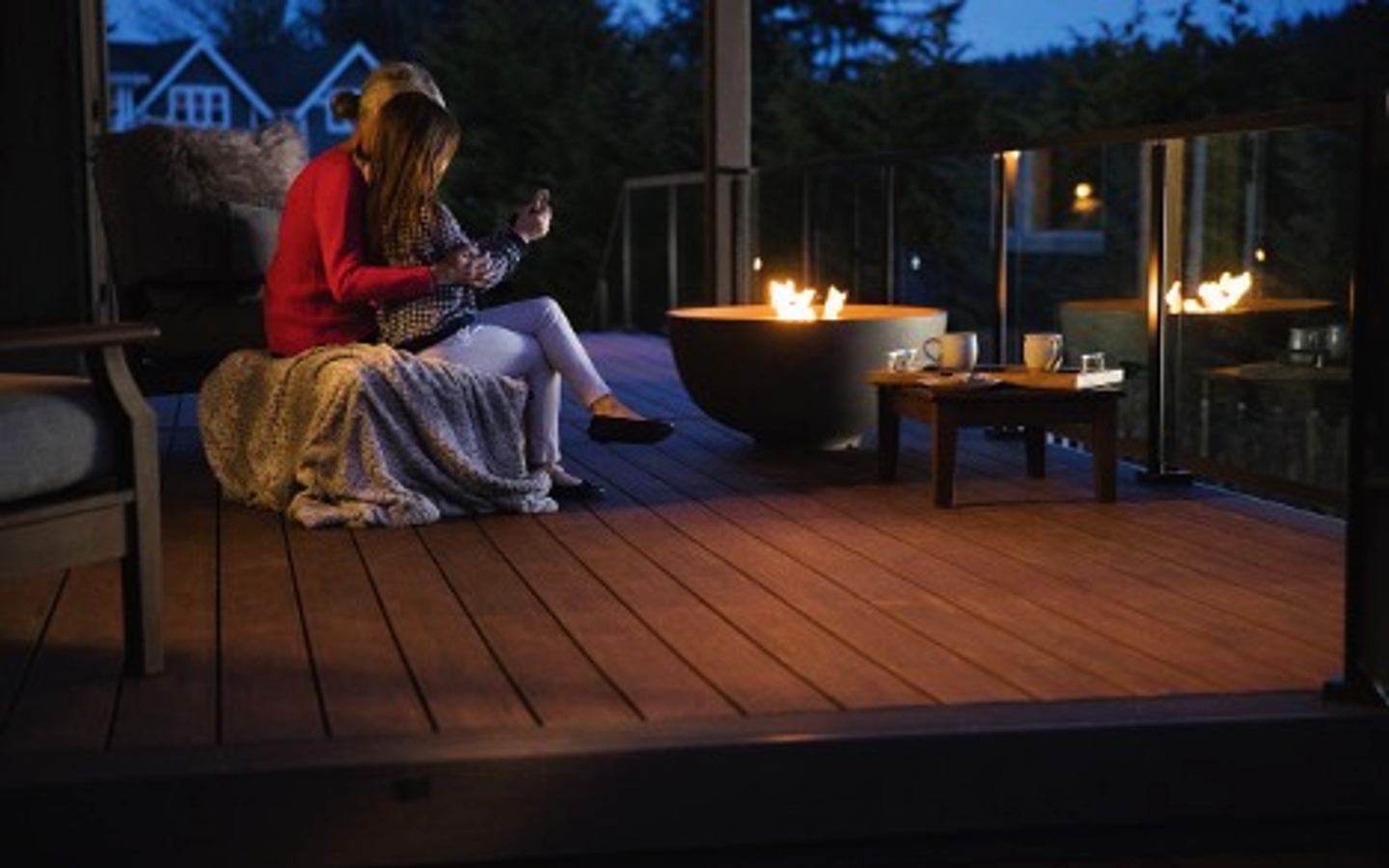 A couple sitting on a deck with a fire pit
Description automatically generated