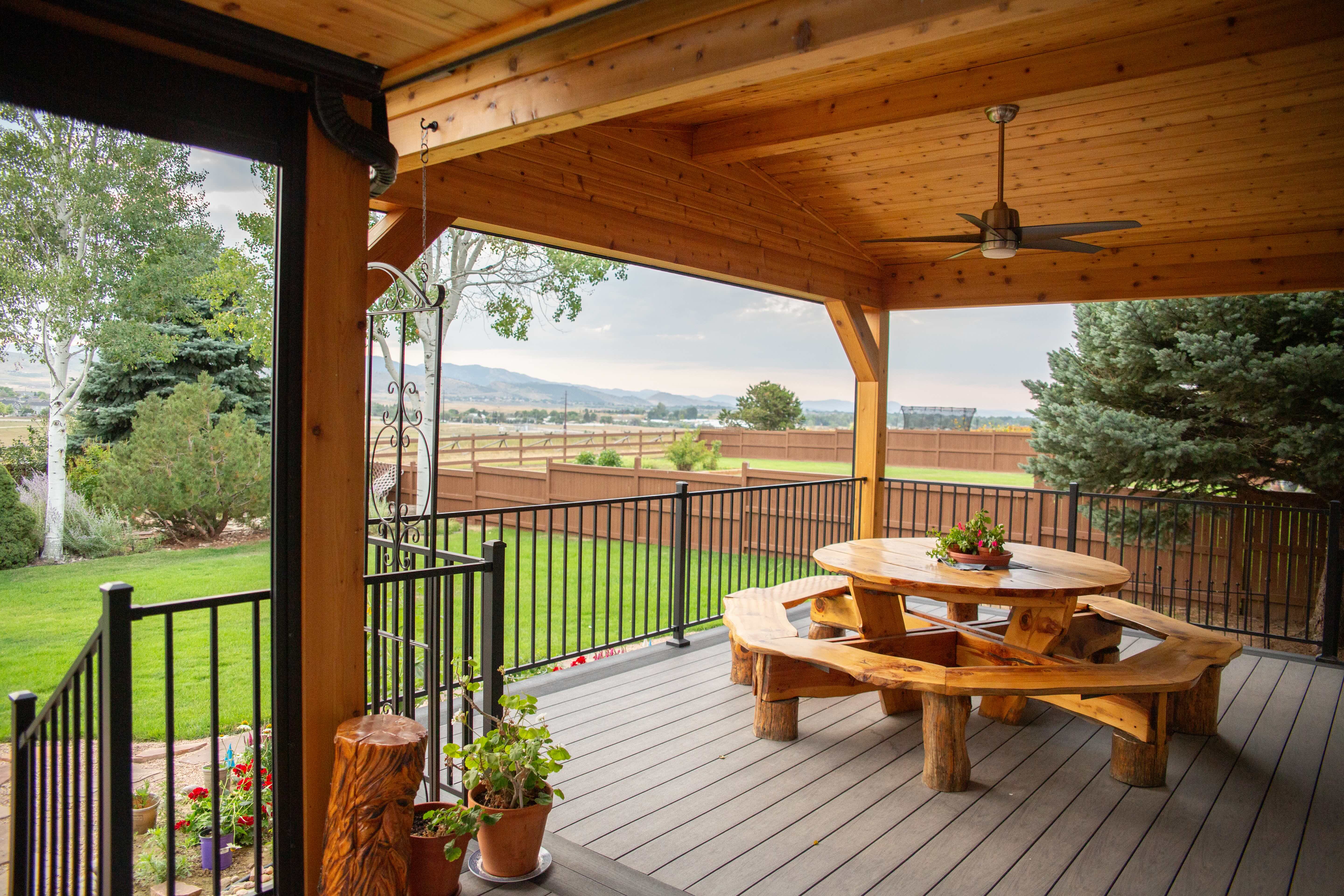 Wood covered patio with black railing and a light colored woof table in center